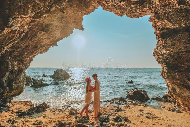 Das Paar, das auf einem Felsen am Eingang der Höhle steht, blickt aufs Meer und bietet einen schönen Blick auf das Meer. bei Sonne lizenzfreie stockfotos