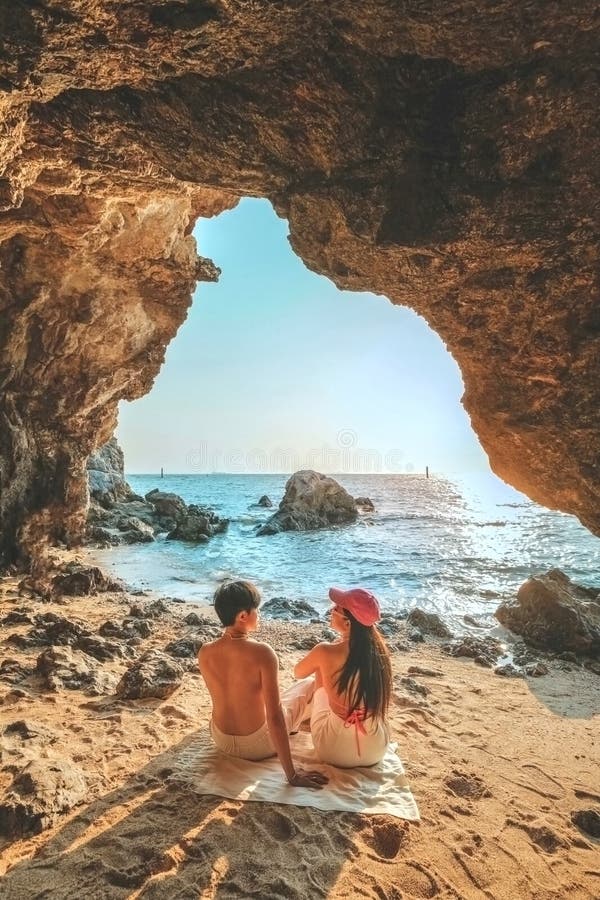 Das Paar, das auf einem Felsen am Eingang der Höhle steht, blickt aufs Meer und bietet einen schönen Blick auf das Meer. bei Sonne stockbilder