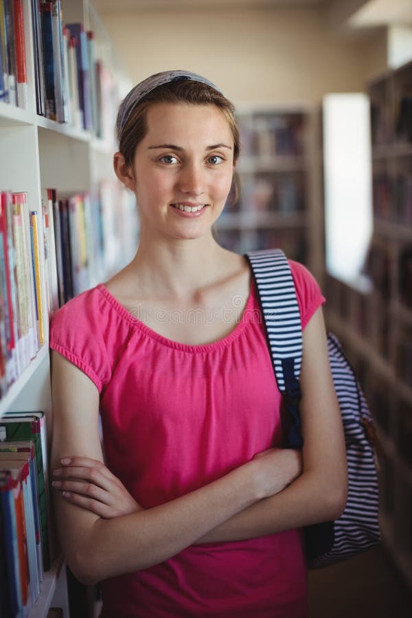 Das Porträt des Schulmädchens stehend mit den Armen kreuzte in der Bibliothek