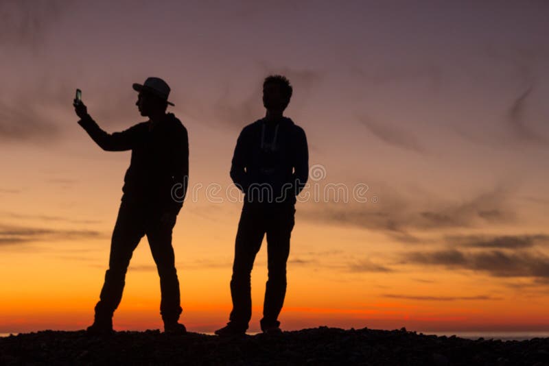 Das Schattenbild von zwei jungen Männern, die Fotos während eines schönen Sonnenuntergangs machen lizenzfreie stockfotos