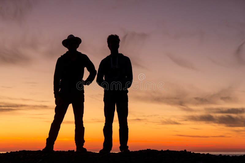 Das Schattenbild von zwei jungen Männern, die zurück zu einem schönen Sonnenuntergang sich drehen lizenzfreies stockfoto