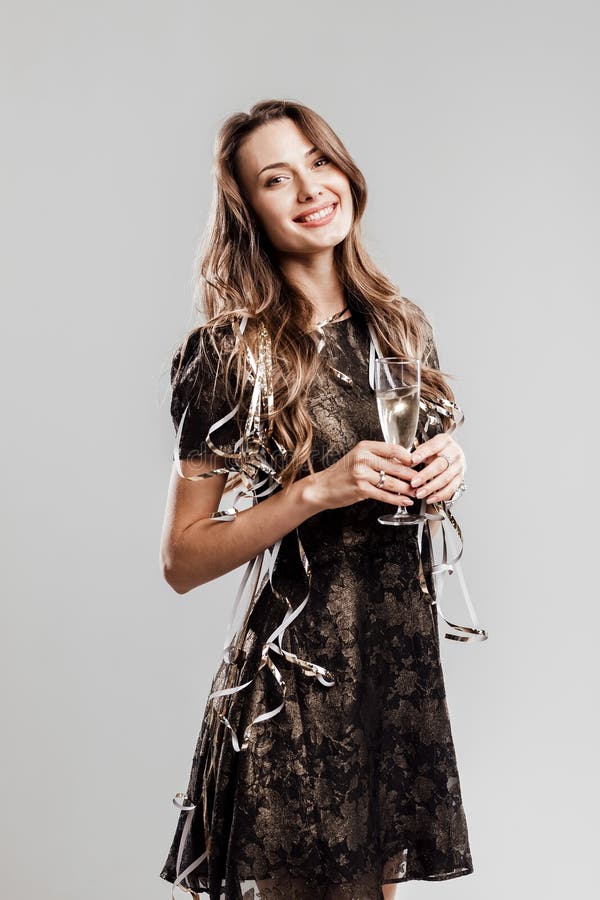 Das schöne Mädchen, das im stilvollen eleganten schwarzen Kleid gekleidet wird, lächelt und hält Gläser Champagner auf einem weiß lizenzfreies stockfoto