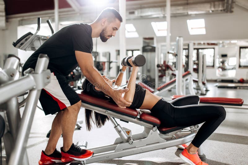 Das schöne athletische Mädchen, das in der schwarzer Sportspitze und -strumpfhosen gekleidet wird, baut Muskeln mit Dummköpfen un lizenzfreies stockfoto