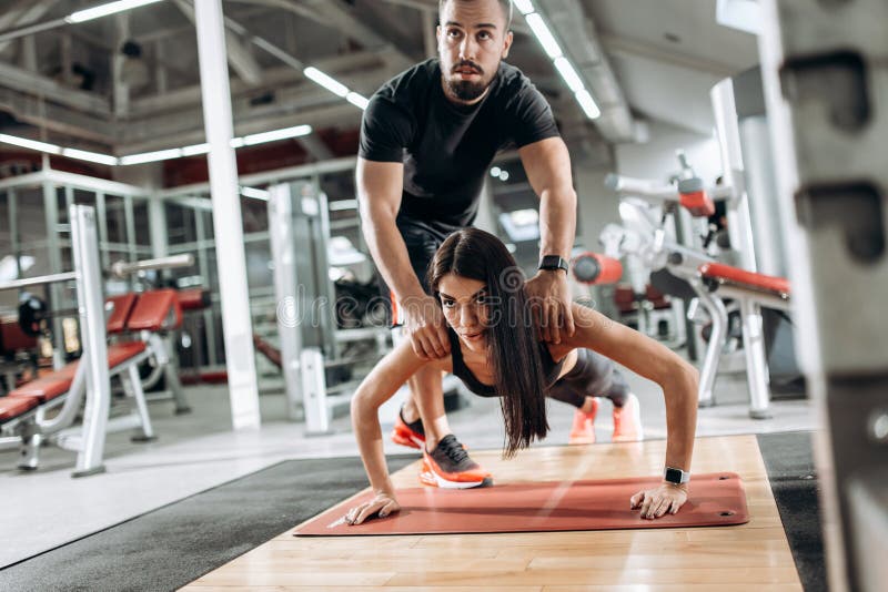 Das schöne athletische Mädchen, das in der schwarzer Sportspitze und -strumpfhosen gekleidet wird, tut Planke und der Trainer kor lizenzfreie stockfotos