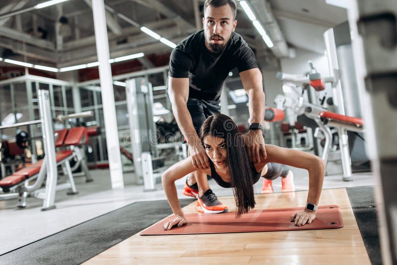 Das schöne athletische Mädchen, das in der schwarzer Sportspitze und -strumpfhosen gekleidet wird, tut Planke und der Trainer kor stockfotografie