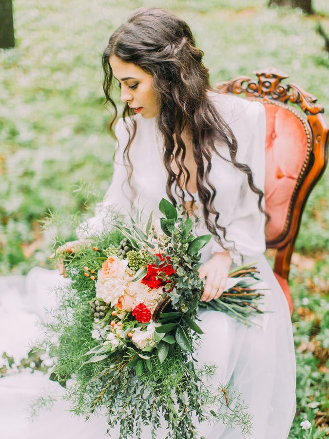 Das Seitenporträt der Frau mit dem langen gelockten Haar im weißen Hochzeitskleid, Holding der bunte Blumenstrauß und stockfoto Das Seitenporträt der Frau mit dem langen gelockten Haar im weißen Hochzeitskleid, Holding der bunte Blumenstrauß und stockfoto