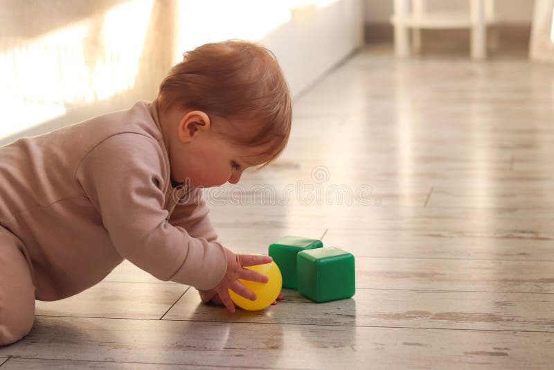 Das süße Baby spielt mit einer Kugel und Spielzeugwürfel zu Hause auf dem Boden. Montessori-Materialien für die Entwicklung von Ki lizenzfreie stockbilder