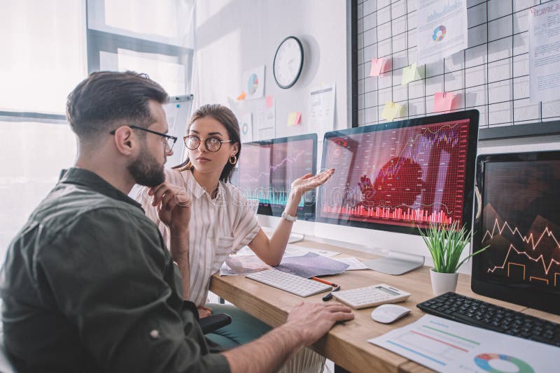 Data analyst pointing with hand at charts on computer monitor to colleague at table royalty free stock image