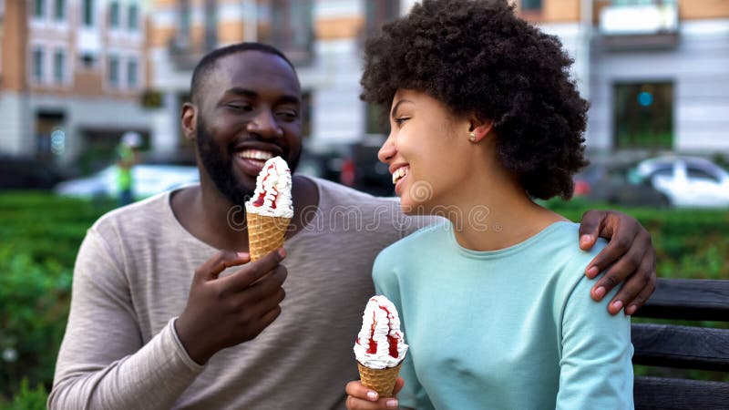 Datando os pares que comem o gelado, sentando-se no banco da cidade, tendo o divertimento junto, amor foto de stock Datando os pares que comem o gelado, sentando-se no banco da cidade, tendo o divertimento junto, amor foto de stock
