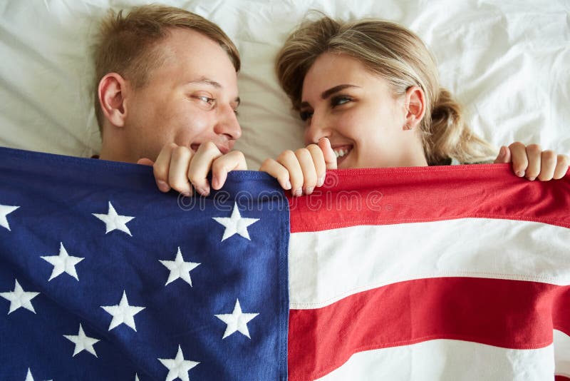 Datas novas felizes que cobrem com a bandeira americana ao encontrar-se na cama foto de stock Datas novas felizes que cobrem com a bandeira americana ao encontrar-se na cama foto de stock