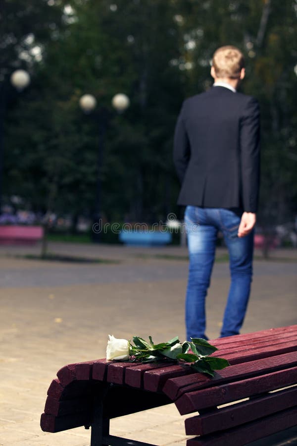 Failed dating. Man walks away. Close up white broken rose on the bench. Failed dating. Man walks away. Close up white broken rose on the bench.