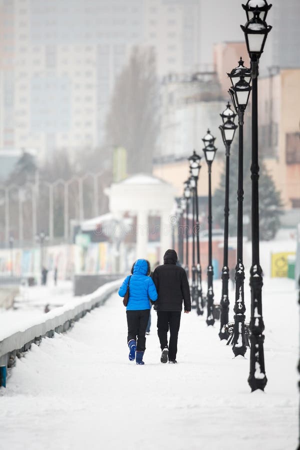 A date in the winter on the waterfront. People walk in the snow on the street. A couple in love