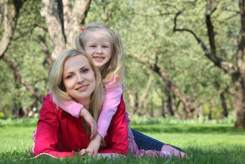 Daughter embraces mother lying on grass