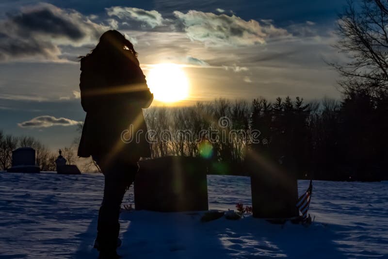 A photo of a mourning daughter at her father`s grave in the cold snow, saying good-byes and thinking about their times together and their time cut short. beautifully silhouetted in the setting sunlight. A daughter`s love knows no end. A photo of a mourning daughter at her father`s grave in the cold snow, saying good-byes and thinking about their times together and their time cut short. beautifully silhouetted in the setting sunlight. A daughter`s love knows no end.