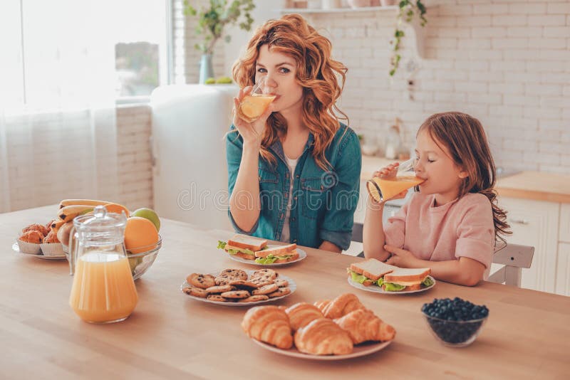 Daughter and mother drinking orange juice for breakfast at domestic kitchen