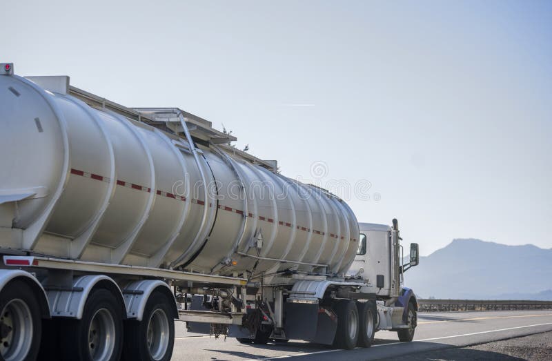 Day cab big rig semi truck transporting liquid cargo in tank semi trailer running on the road in sunny day