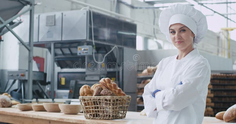 De aantrekkelijke commerciële grote glimlach van de vrouwenbakker in een bakkersbedrijf die recht van cameraclose-up het dragen k