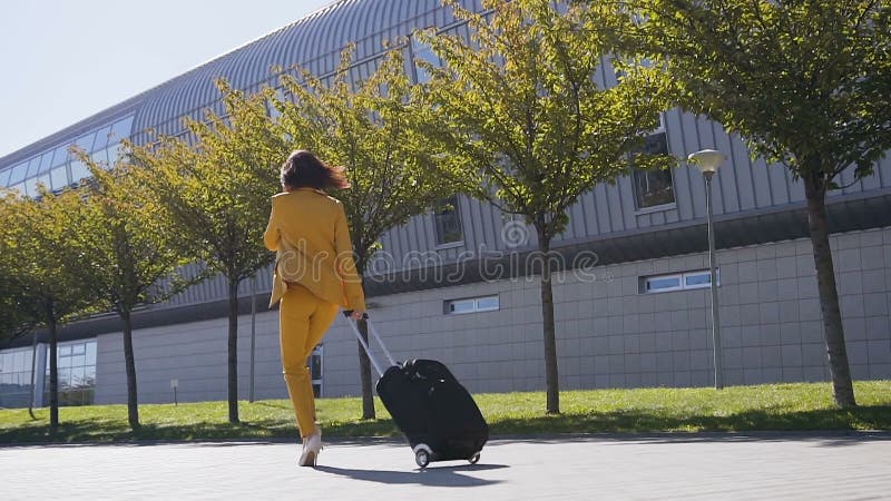 De aantrekkelijke jonge bedrijfsvrouw in een formeel Kostuum trekt een Koffer, die op haar smartphone spreken, haast zich aan zak