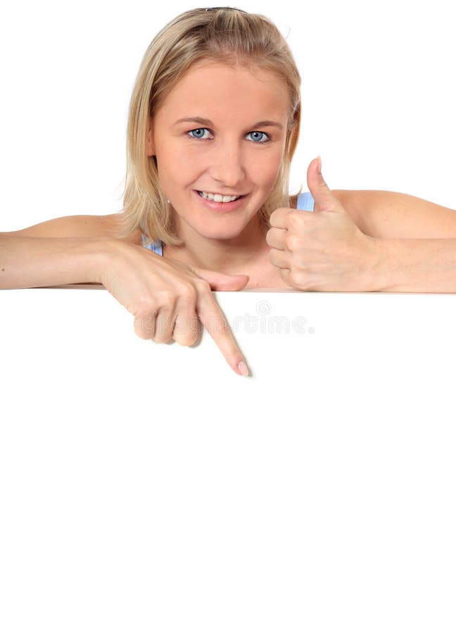 Attractive young woman showing thumbs up while pointing down blank white sign. All on white background. Attractive young woman showing thumbs up while pointing down blank white sign. All on white background.