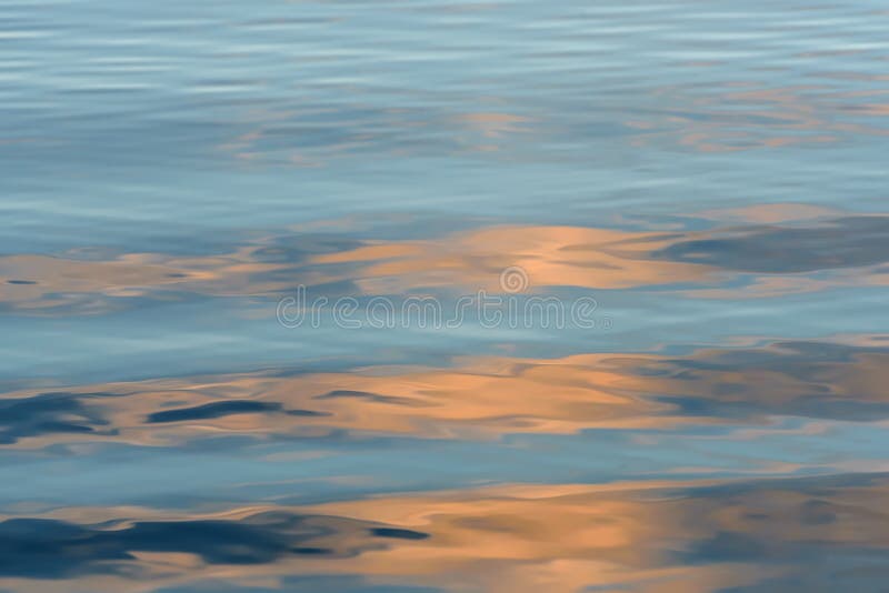 Abstract natural background with reflections of sky and clouds and a beautiful soft waves on the blue water of the lake at sunset. Abstract natural background with reflections of sky and clouds and a beautiful soft waves on the blue water of the lake at sunset