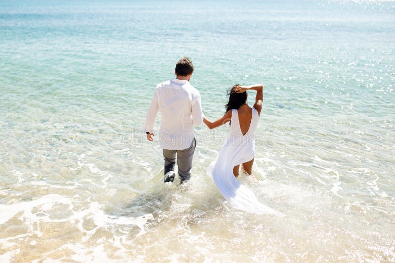 De achtermening van een jong enkel echtpaar twee gaat in kleding in water, de zomertijd, vakantie in Griekenland binnen honeymoon royalty-vrije stock afbeeldingen De achtermening van een jong enkel echtpaar twee gaat in kleding in water, de zomertijd, vakantie in Griekenland binnen honeymoon royalty-vrije stock afbeeldingen