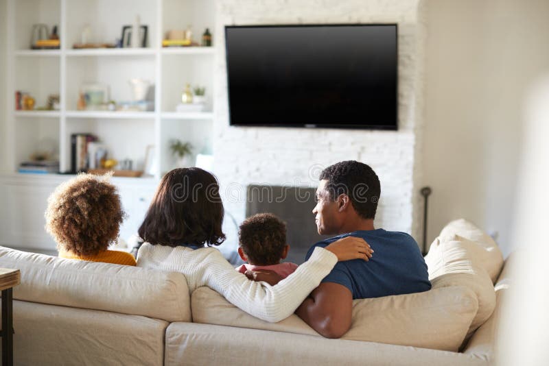 De achtermening van jonge familiezitting op de bank en het letten op TV samen in hun woonkamer, sluit omhoog