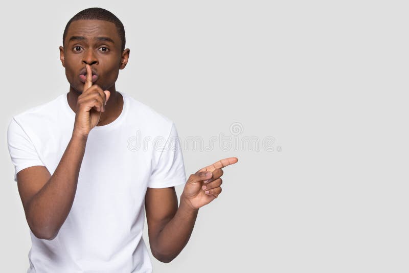 African american man holding finger on lip mouth keep it quiet hush secret pointing at copy space aside isolated on white grey blank studio background, black guy showing shh shush gesture for silence. African american man holding finger on lip mouth keep it quiet hush secret pointing at copy space aside isolated on white grey blank studio background, black guy showing shh shush gesture for silence