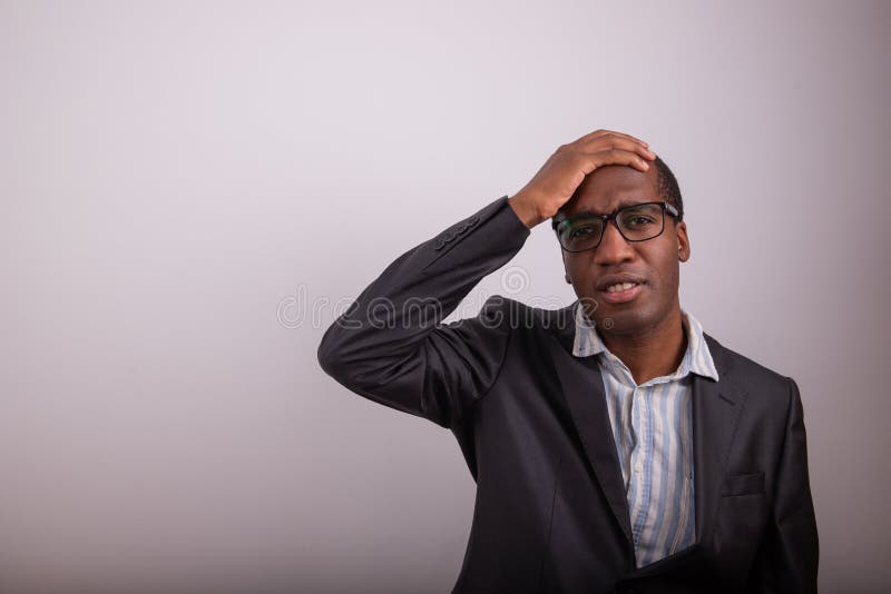 African businessman has a confused expression, he puts his hand on his head and is disoriented. Man with eyeglasses and lost expression, copy space on the person`s left. African businessman has a confused expression, he puts his hand on his head and is disoriented. Man with eyeglasses and lost expression, copy space on the person`s left