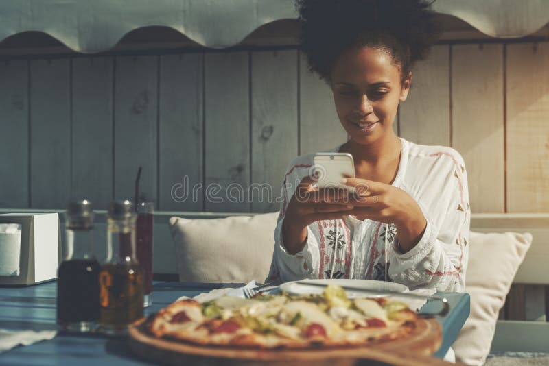 De Afrovrouw schiet pizza op haar cellphone stock afbeelding De Afrovrouw schiet pizza op haar cellphone stock afbeelding