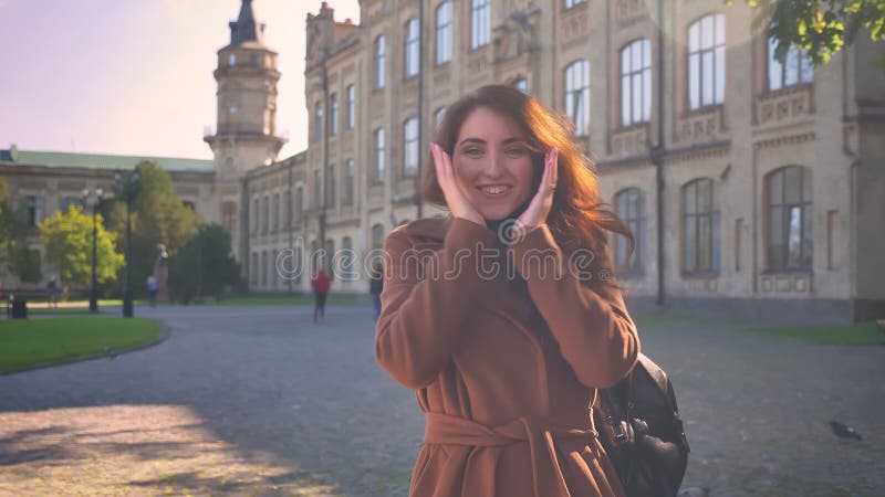 De artistieke emotionele donkerbruine Kaukasische vrouw is demonstratie zoals tekens bij camera en het glimlachen natuurlijk terw