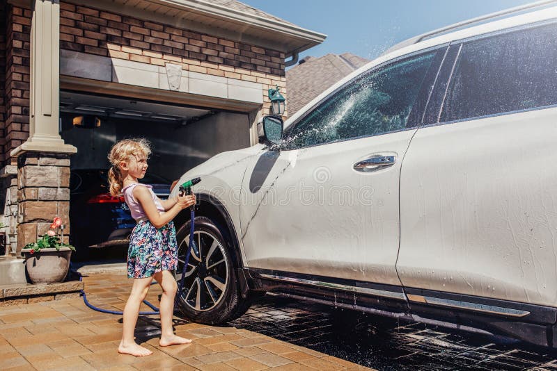 De auto van de meisjeswas op oprijlaan vooraan huis op zonnige de zomerdag stock fotografie De auto van de meisjeswas op oprijlaan vooraan huis op zonnige de zomerdag stock fotografie