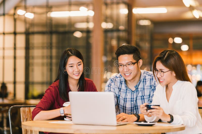 De Aziatische studenten groeperen zich of medewerkers samen gebruikend laptop computer bij koffie of universiteit Toevallige zake