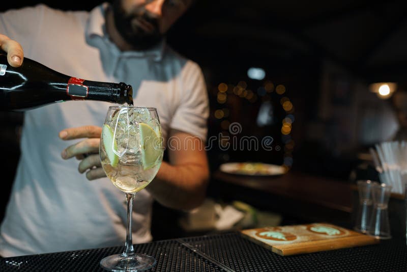 De barman giet champagne van een fles in een glas bij een nachtclub bij de bar Professionele barman die een cocktail maken levens stock afbeelding De barman giet champagne van een fles in een glas bij een nachtclub bij de bar Professionele barman die een cocktail maken levens stock afbeelding
