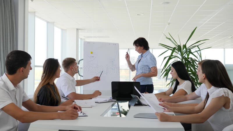 De beambte op zaken komt toont van diagram op Whiteboard voor collega's in bestuurskamer samen