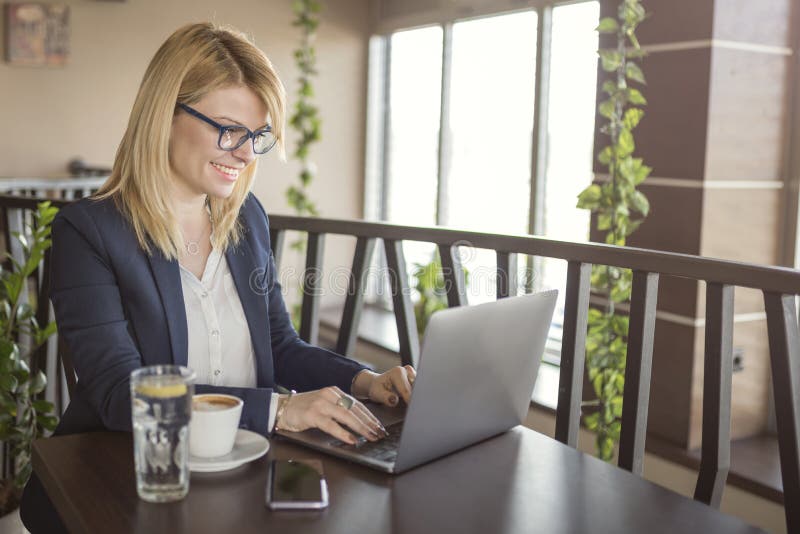 De bedrijfsvrouw werkt aan computer en het drinken kop van koffie en glas water in een koffiewinkel, restaurant royalty-vrije stock afbeelding De bedrijfsvrouw werkt aan computer en het drinken kop van koffie en glas water in een koffiewinkel, restaurant royalty-vrije stock afbeelding