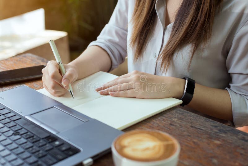 De bedrijfsvrouwen die laptop met behulp van en nemen nota van sommige gegevens over blocnote stock fotografie De bedrijfsvrouwen die laptop met behulp van en nemen nota van sommige gegevens over blocnote stock fotografie