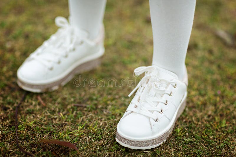 De benen van kinderen in witte tennisschoenen die zich op het groene gras bevinden openlucht royalty-vrije stock foto De benen van kinderen in witte tennisschoenen die zich op het groene gras bevinden openlucht royalty-vrije stock foto