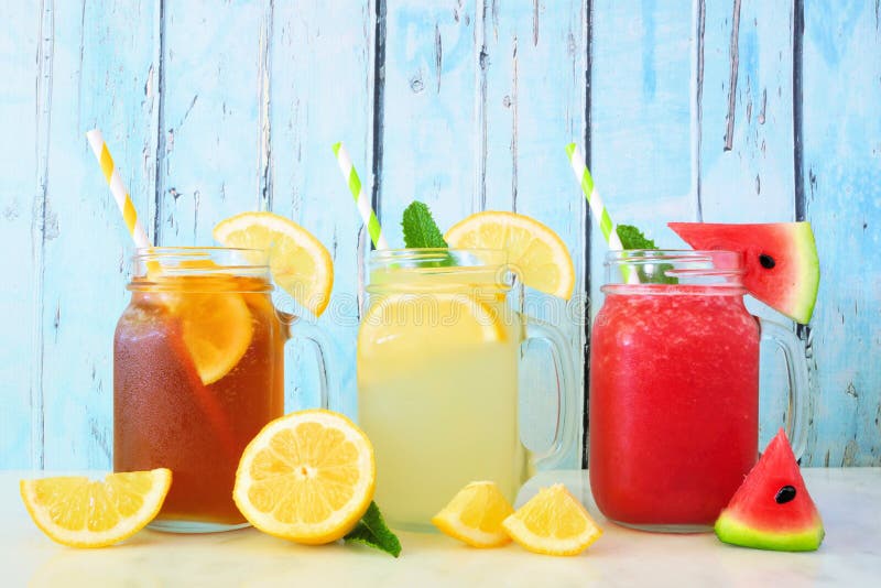 De bevroren thee, limonade en watermeloendranken van de sapzomer in de glazen van de metselaarkruik tegen blauw hout stock fotografie De bevroren thee, limonade en watermeloendranken van de sapzomer in de glazen van de metselaarkruik tegen blauw hout stock fotografie