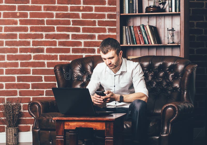 De bezige mens roept een telefoonaantal De zakenman is in zijn kabinet achter zijn laptop op de achtergrond van muur met decorati stock afbeeldingen De bezige mens roept een telefoonaantal De zakenman is in zijn kabinet achter zijn laptop op de achtergrond van muur met decorati stock afbeeldingen