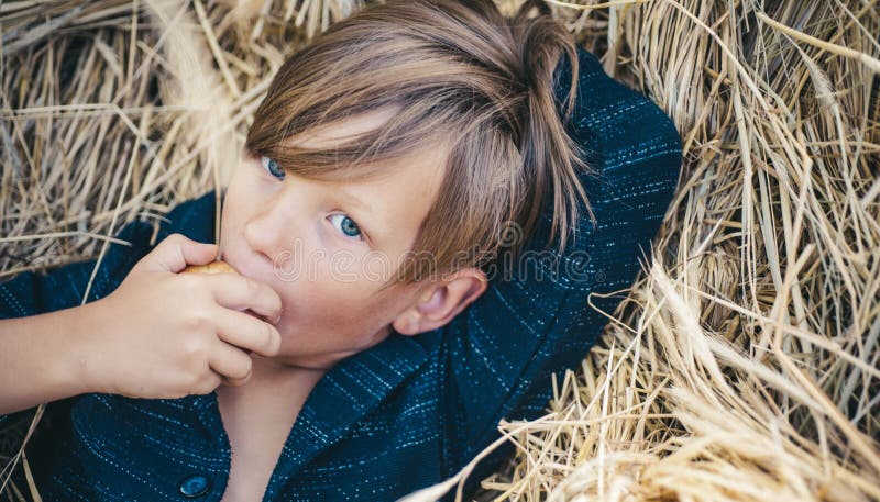 De blonde jongen ligt op hooiachtergrond en eet een appel De jongen adverteert kinderen` s kleren voor de herfst gelukkig royalty-vrije stock afbeeldingen De blonde jongen ligt op hooiachtergrond en eet een appel De jongen adverteert kinderen` s kleren voor de herfst gelukkig royalty-vrije stock afbeeldingen
