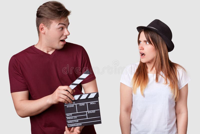 De boze vrouw in modieus hoofddeksel bekijkt haar producent die clapperboard, heeft geschokt uitdrukking, voorstelt nieuwe geconc royalty-vrije stock fotografie De boze vrouw in modieus hoofddeksel bekijkt haar producent die clapperboard, heeft geschokt uitdrukking, voorstelt nieuwe geconc royalty-vrije stock fotografie