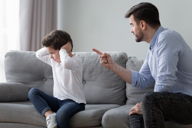 Angry young dad sit on couch lecture scold preschooler son closing ears with hands, offended stubborn boy child avoid ignore listening to serious mad father talking, having dispute or quarrel at home. Angry young dad sit on couch lecture scold preschooler son closing ears with hands, offended stubborn boy child avoid ignore listening to serious mad father talking, having dispute or quarrel at home