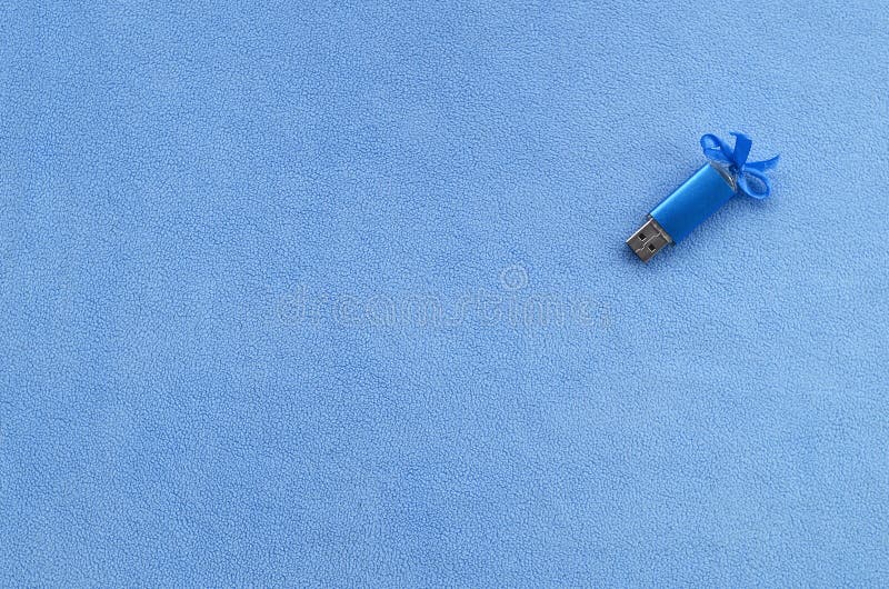 De briljante blauwe het geheugenkaart van de usbflits met een blauwe boog ligt op een deken van zachte en bont lichtblauwe vachts stock foto De briljante blauwe het geheugenkaart van de usbflits met een blauwe boog ligt op een deken van zachte en bont lichtblauwe vachts stock foto