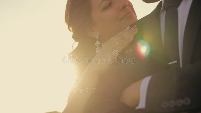 De bruidegom omhelst de bruid in een park in de zonneschijn