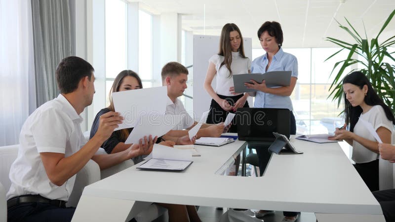 De bureaumensen met in hand documenten spreken samenkomen in moderne bestuurskamer in Commercieel centrum