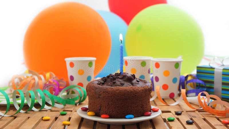 De cake van de chocoladeverjaardag met een blauwe kaars die op rustieke houten lijst met achtergrond van kleurrijke ballons, gift royalty-vrije stock foto's De cake van de chocoladeverjaardag met een blauwe kaars die op rustieke houten lijst met achtergrond van kleurrijke ballons, gift royalty-vrije stock foto's