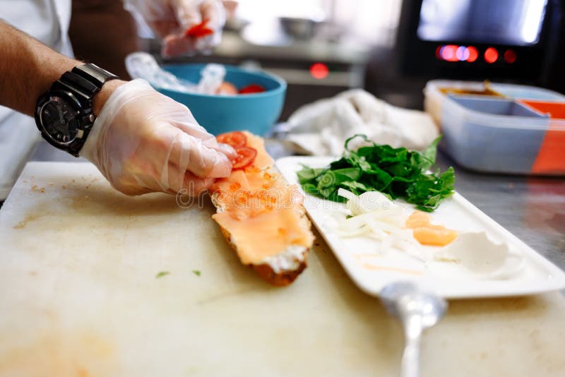De chef-kok bereidt een baguette met zalm op een witte raad voor royalty-vrije stock foto's De chef-kok bereidt een baguette met zalm op een witte raad voor royalty-vrije stock foto's