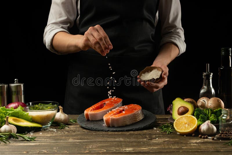 De chef-kok bereidt verse zalmvissen voor, smorguforel, die zout bestrooien met de ingrediënten Vorst het bevriezen in de lucht H stock fotografie De chef-kok bereidt verse zalmvissen voor, smorguforel, die zout bestrooien met de ingrediënten Vorst het bevriezen in de lucht H stock fotografie
