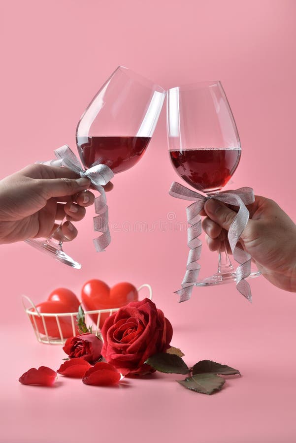 De Clinkingsglazen rode wijn in handen, met rood namen op de bodem op roze achtergrond toe Concept de Dag van Valentine ` s stock foto De Clinkingsglazen rode wijn in handen, met rood namen op de bodem op roze achtergrond toe Concept de Dag van Valentine ` s stock foto
