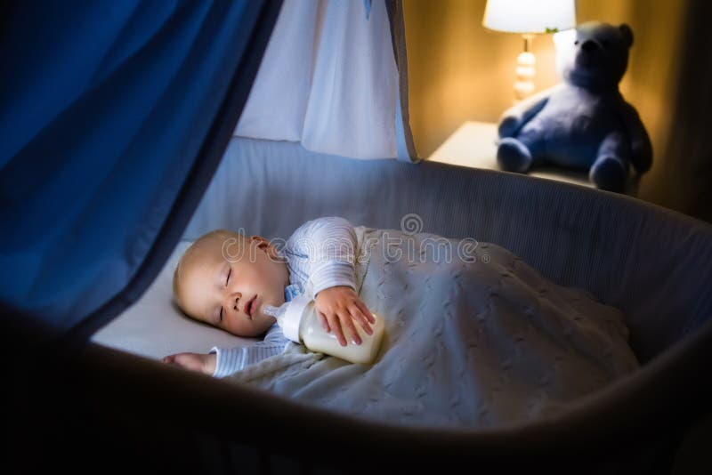 De consumptiemelk van de babyjongen in bed stock fotografie De consumptiemelk van de babyjongen in bed stock fotografie